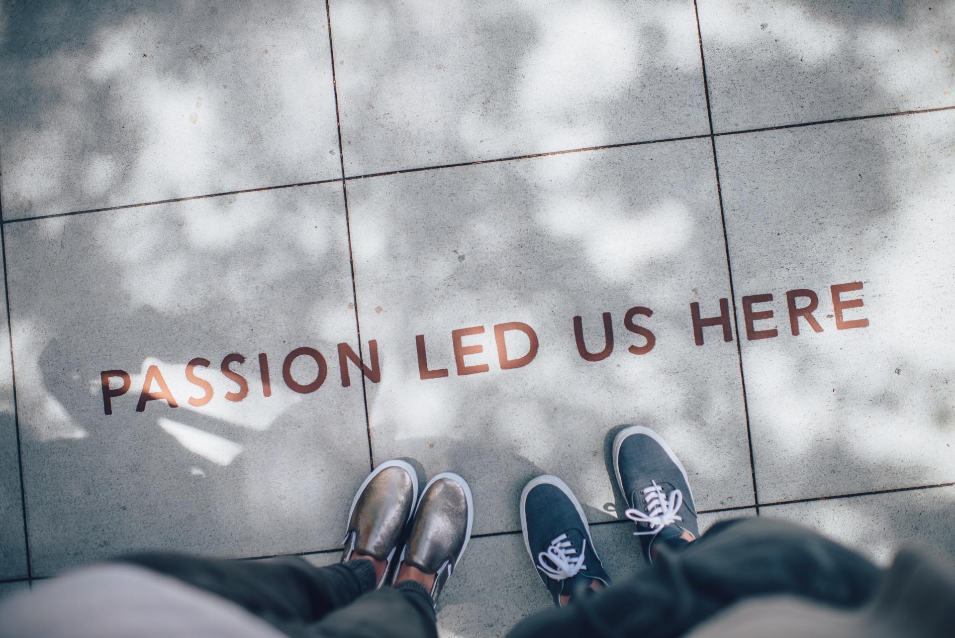 Feet of two people on tiled pavement painted with the words passion led us here