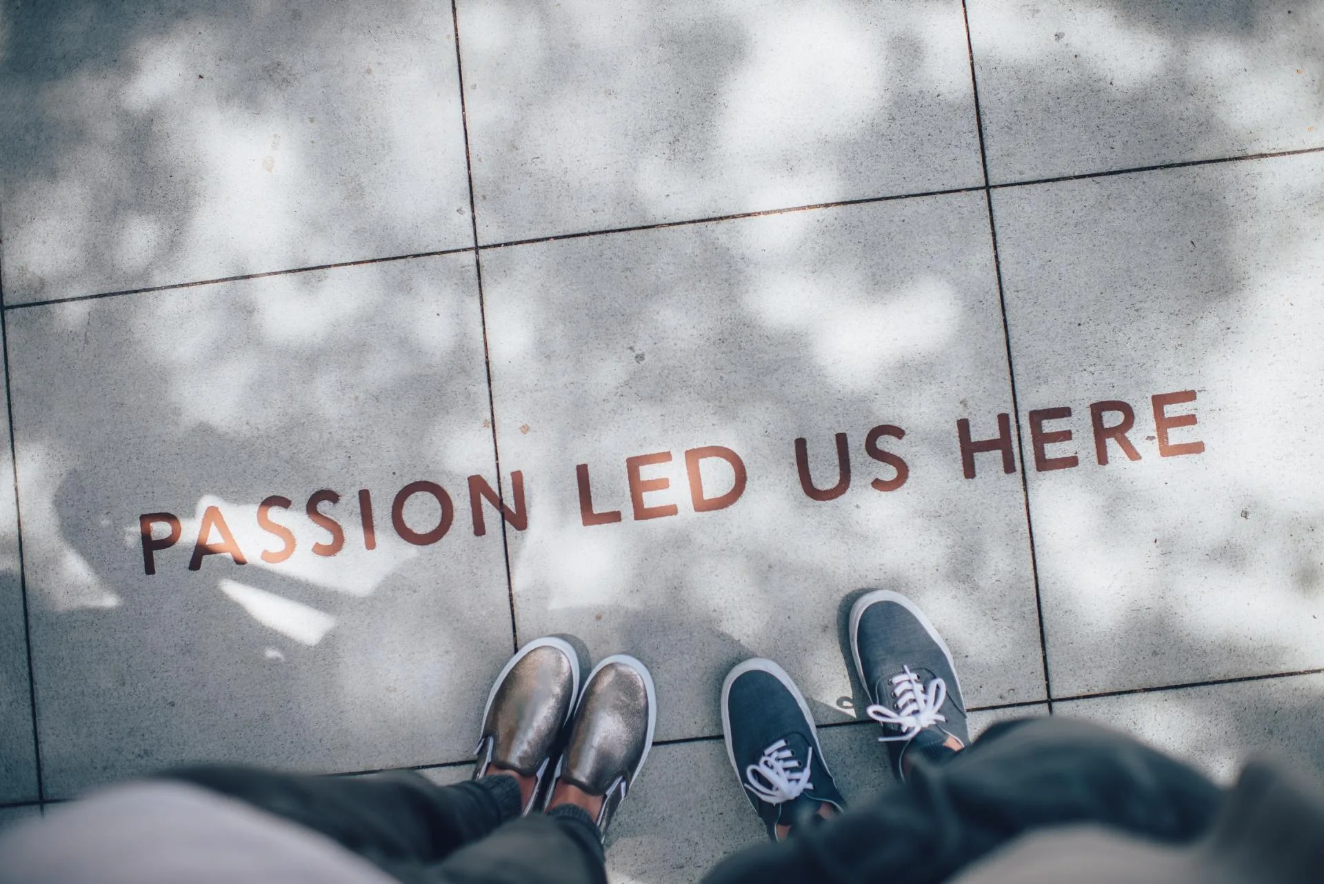 Feet of two people on tiled pavement painted with the words passion led us here