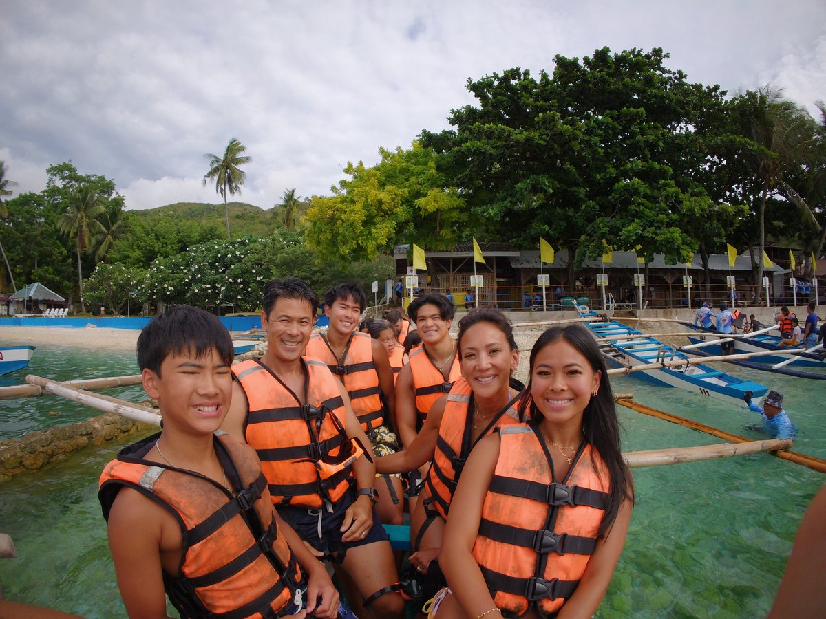 The family wearing life vests on an outrigger boat over turquoise water in the Philippines